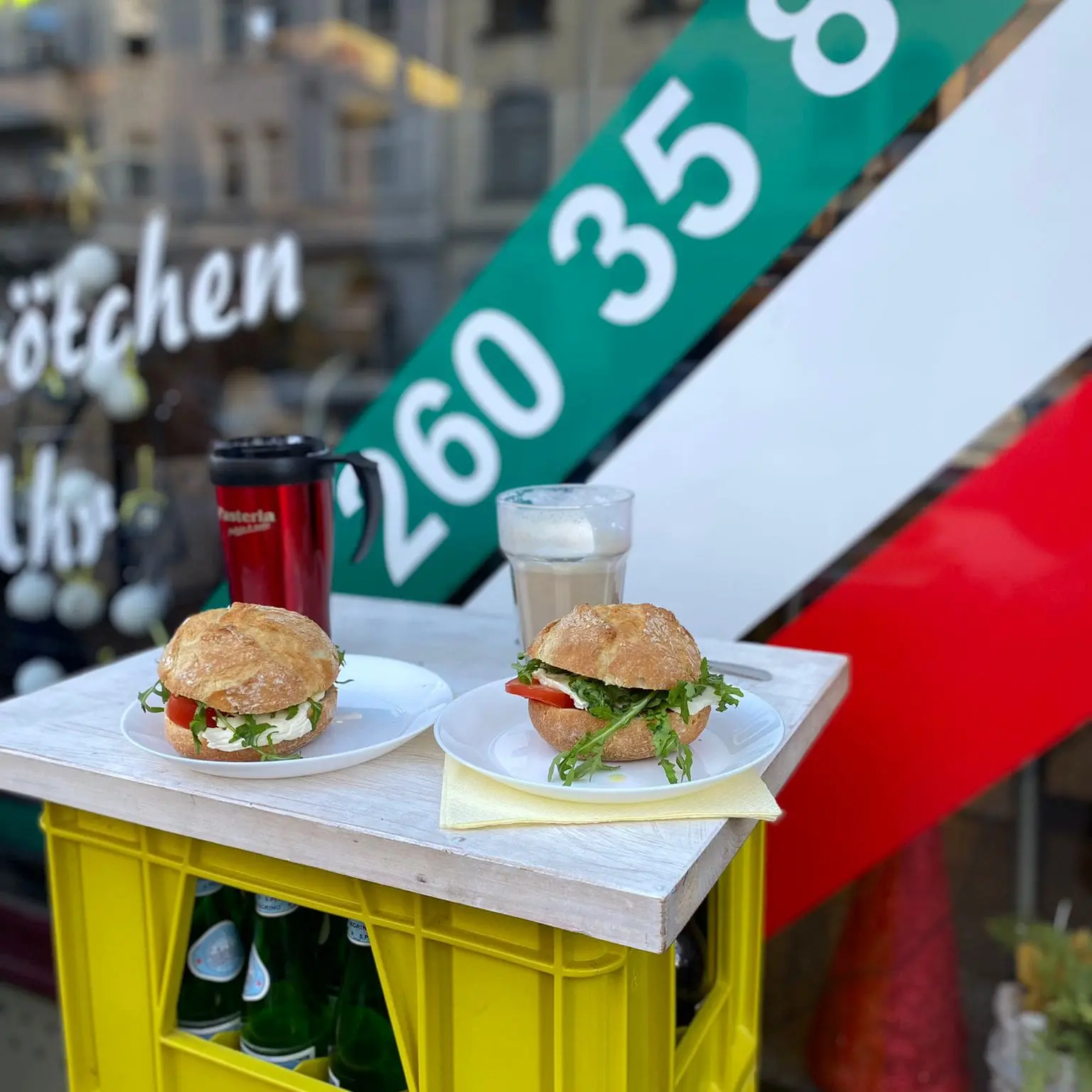 Stehtisch mit zwei belegten Brötchen und Getränken vor der Pasteria