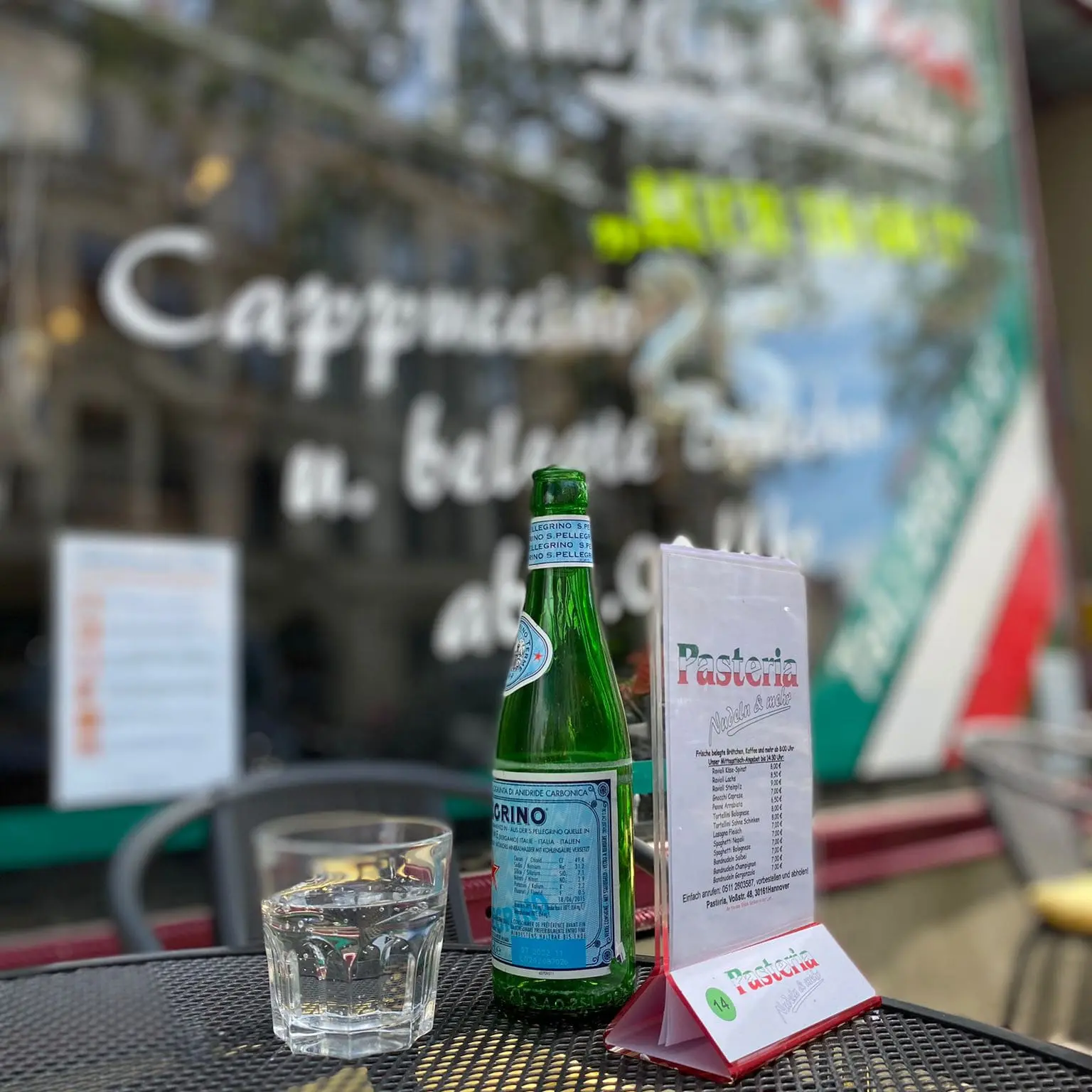 Ein Glas mit einer Flasche Pellegrino auf einem Tisch vor der Pasteria